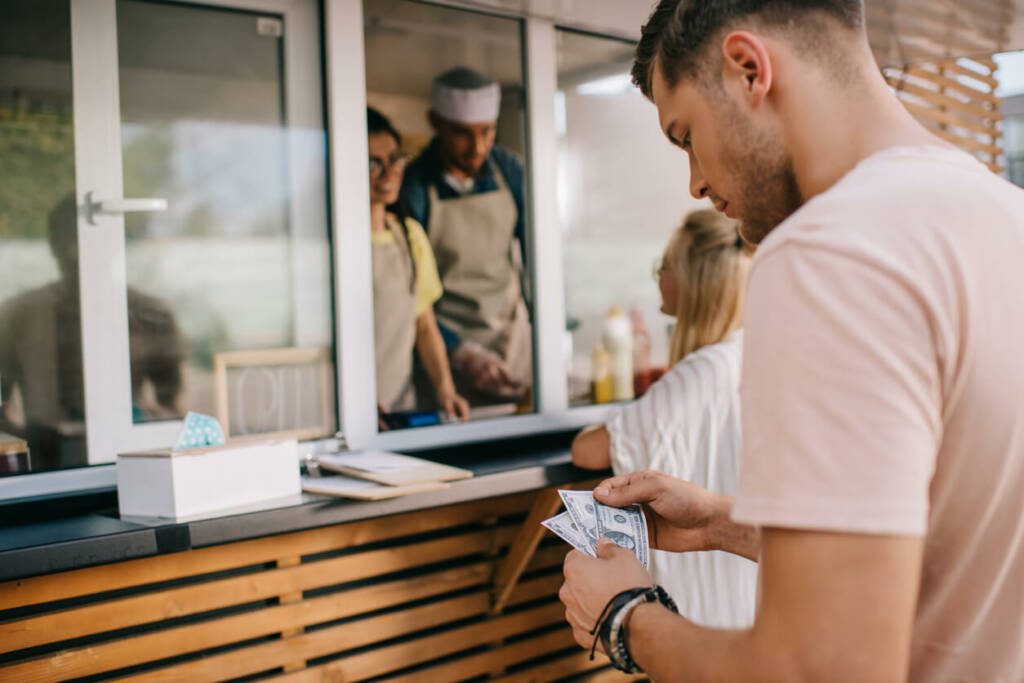 Man in line at restaurant, counting cash in hand.