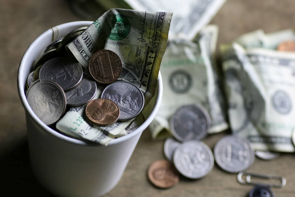 American dollars and coins filling a cup and laying on a table