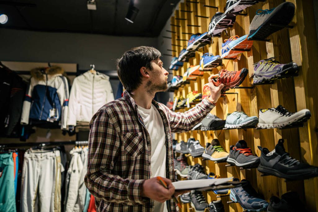 Man looking at a wall of shoes, comparing one shoe to information on a clipboard.