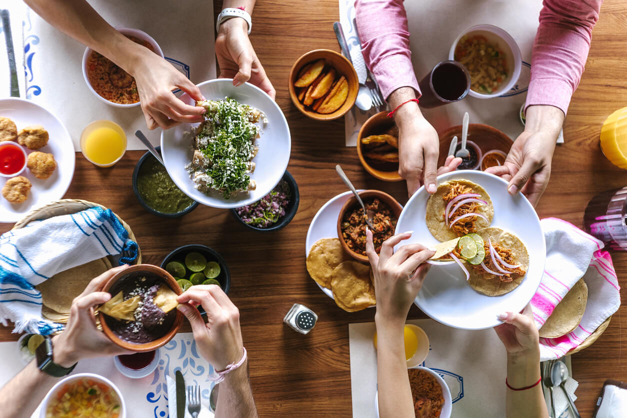 People passing each other plates of Mexican food like tacos and salsa