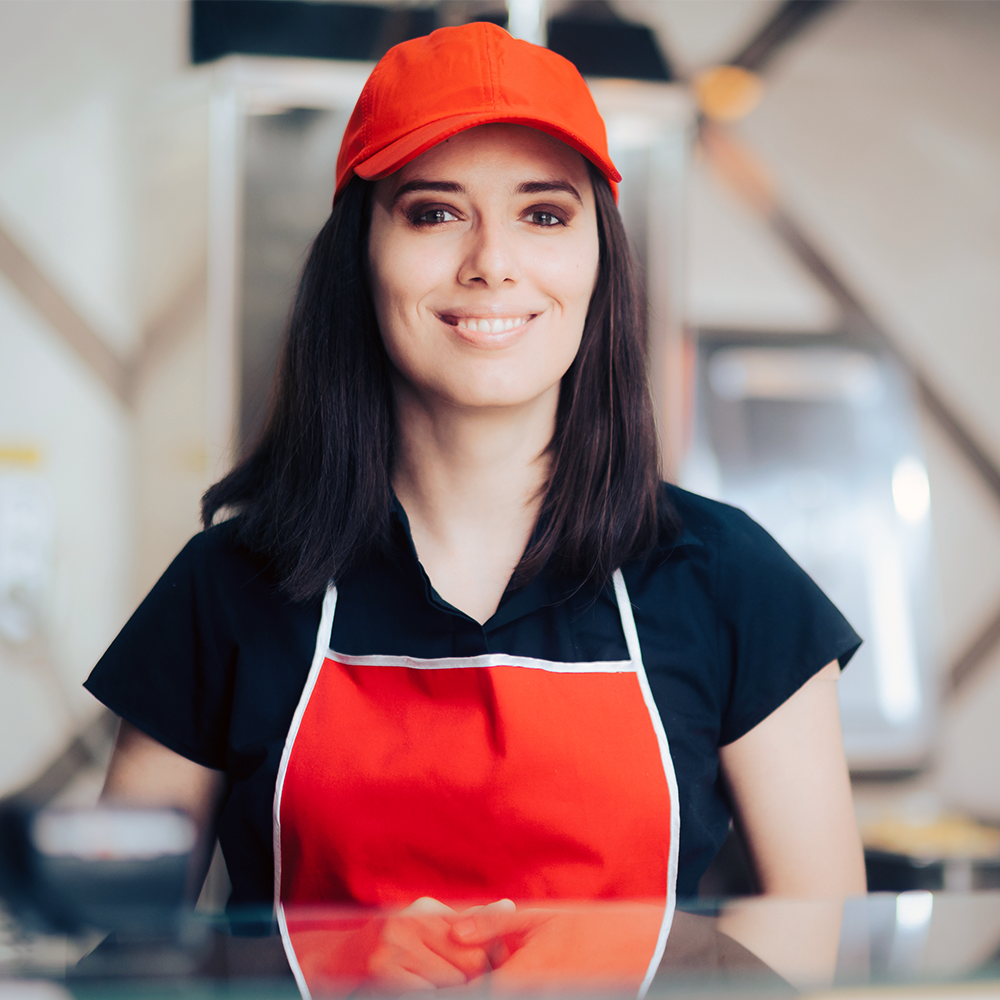 A woman in a black shirt with a red hat and apron who could be a fast food manager