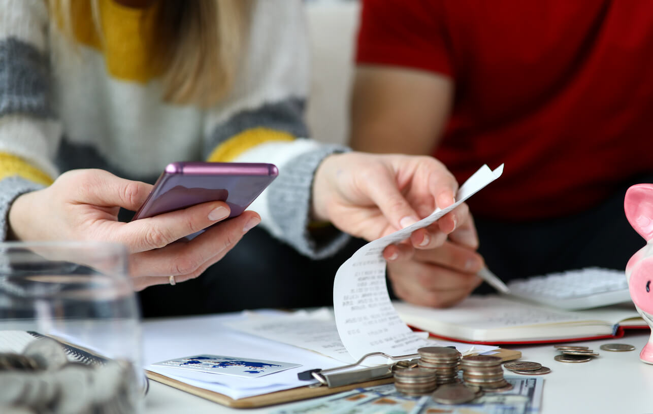 couple reviewing bills and statements with pile of cash and change nearby