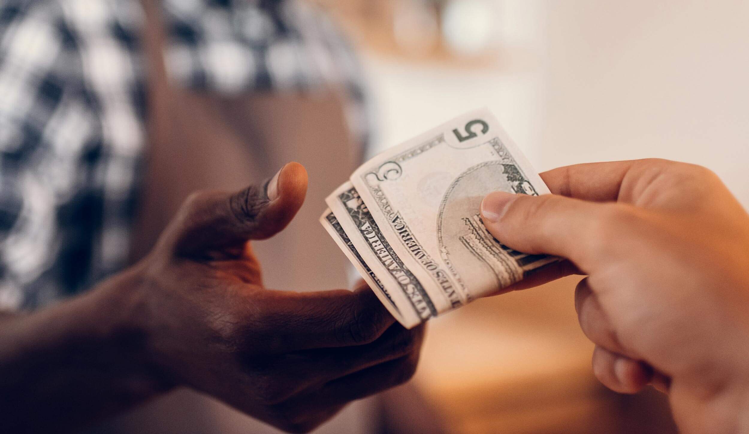 person handing cash for payment to a cashier